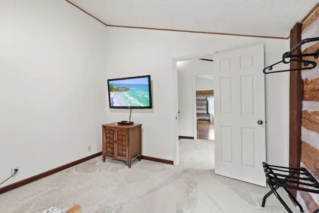 A room with a television on a wooden cabinet, a white door, and a black metal rack.