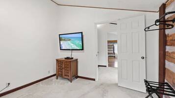 A room with a television on a wooden cabinet, a white door, and a black metal rack.