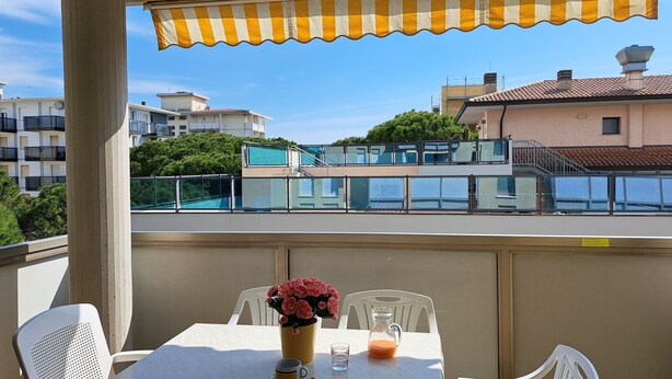 A balcony with a table, chairs, a vase with flowers, and a pitcher of orange juice.