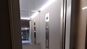 An elevator interior with a metallic finish, a control panel with buttons, and a red emergency light.