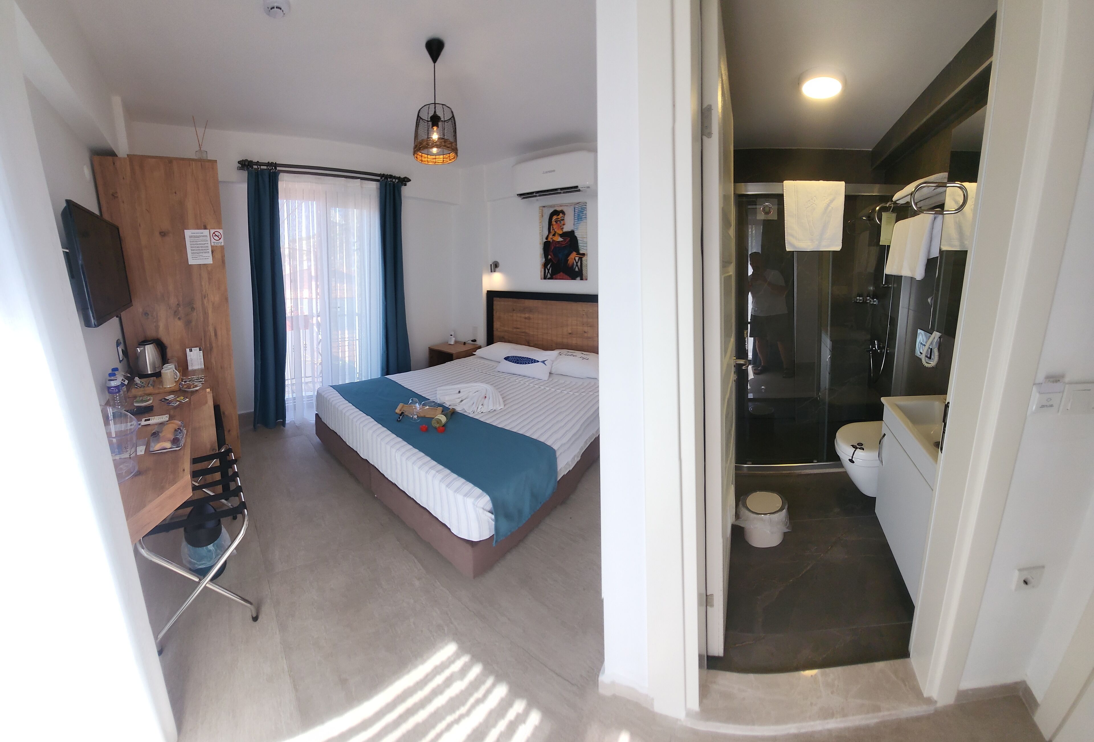 Quarto de hotel com cama, mesa de cabeceira e área de chuveiro.