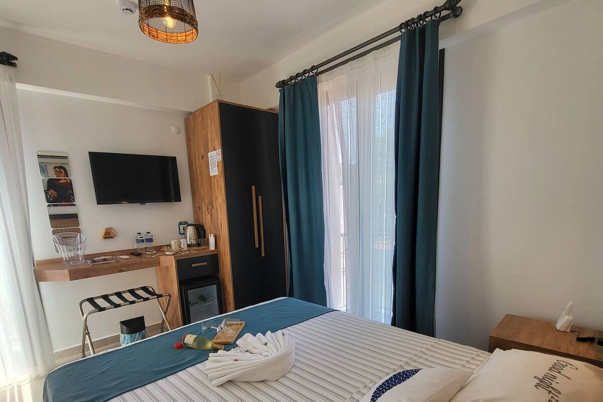A hotel room with a bed, a desk, a chair, a TV, and a window with curtains.