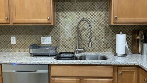 A kitchen with wooden cabinets, a stainless steel dishwasher, a granite countertop, a sink with a faucet, and a tiled backsplash. - Serene Townhome minutes away from Christiana Mall, DE Race Park and Univ. of DE (Newark)