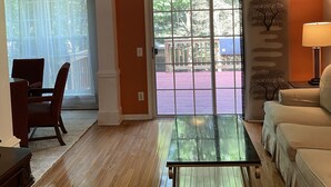 A living room with a glass-top coffee table, a sofa, and a dining area with chairs. - Serene Townhome minutes away from Christiana Mall, DE Race Park and Univ. of DE (Newark)