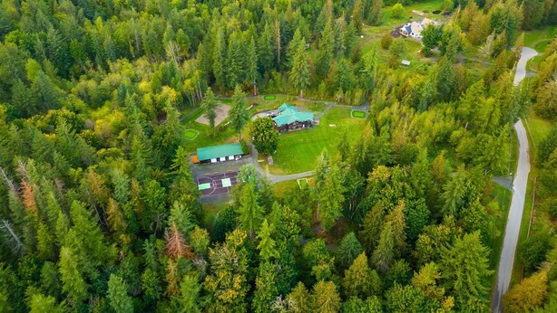 An aerial view of a forested area with a large building featuring a green roof, surrounded by dense trees and a clear road.