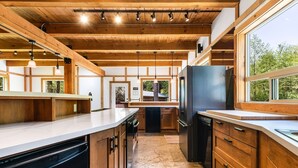 A modern kitchen with wooden beams, large windows, and a view of the outdoors.