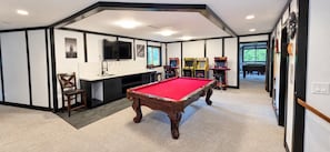 Una mesa de billar en una sala con área de cocina, juegos de arcade y un piano.