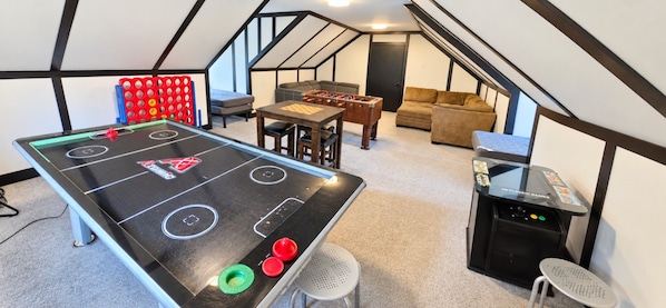 Una habitación con mesa de fútbol de mesa, mesa de ping pong y una consola de videojuegos clásica.