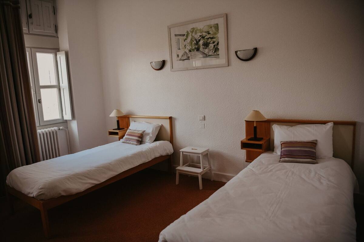Une chambre d’hôtel avec deux lits simples, une petite table et un radiateur.