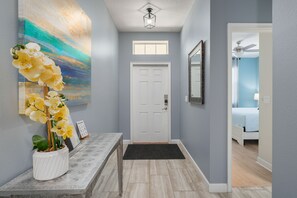 A hallway with a white door, a bench, a potted orchid, and a painting on the wall. - Walk to Clubhouse | Tron Game Room | Tiki Bar | Private Pool | 7BR Villa (Kissimmee)