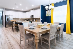 Une cuisine moderne avec des meubles blancs, un réfrigérateur en acier inoxydable et un coin repas comprenant une table et des chaises en bois.