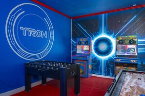 Una habitación con mesa de fútbolín, máquinas de videojuegos y una pared con un logotipo circular grande.