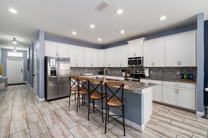 A modern kitchen with white cabinets, stainless steel appliances, and a granite countertop. - Walk to Clubhouse | Tron Game Room | Tiki Bar | Private Pool | 7BR Villa (Kissimmee)