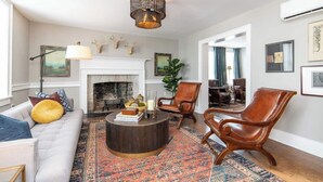 Un salon avec une cheminée, des fauteuils en cuir, une table basse ronde et un tapis à motifs.