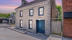 Un bâtiment en pierre de deux étages, avec une porte et des fenêtres bleues, situé à un angle de rue.
