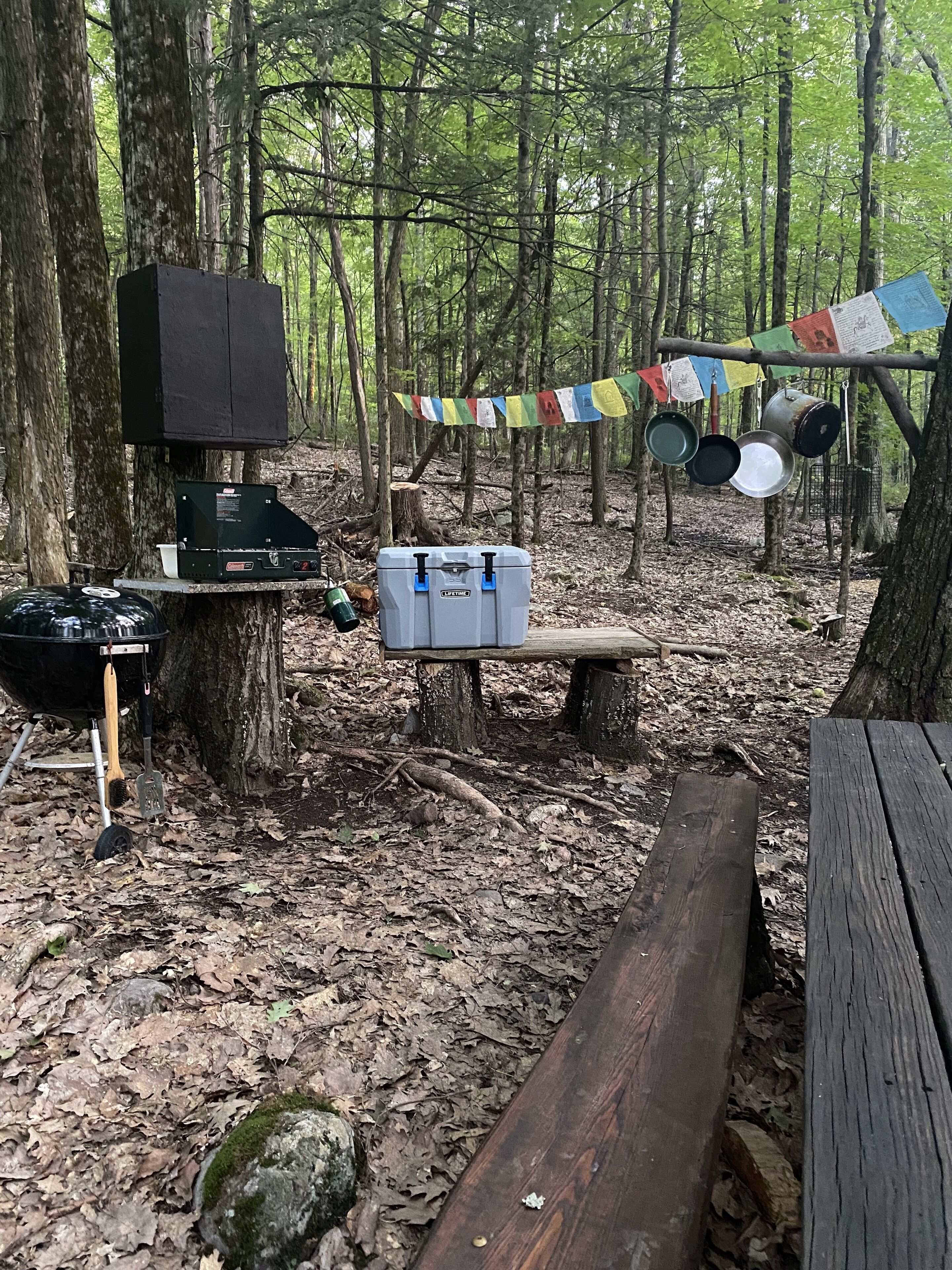 Un terrain de camping équipé d’un barbecue portable, d’une glacière et de matériel de camping.