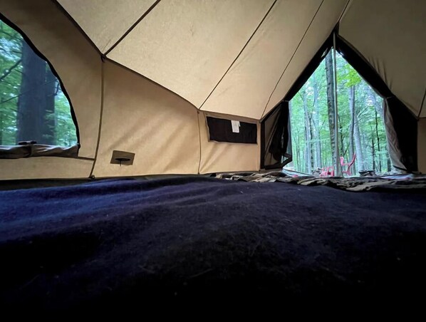 A tent with a sleeping area, a small window, and a view of trees.