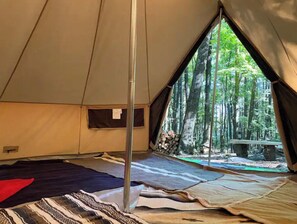 Experience the serene forest surroundings from the comfort of this cozy tent, featuring a large window and plush mats and blankets.