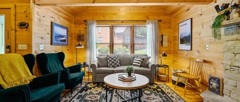 A cozy log cabin interior with a sofa, two armchairs, a coffee table, and a patterned rug.