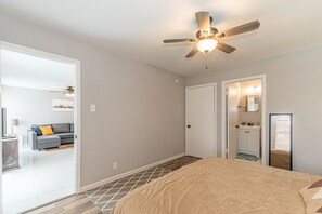 A bedroom with a bed, a ceiling fan, a door leading to a bathroom, and a small seating area with a sofa and a TV. - A SA Pearl (San Antonio)