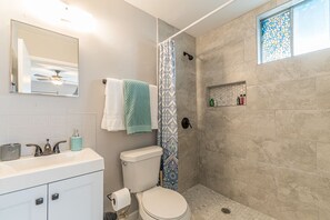 A bathroom with a shower, toilet, sink, and a small window with a stained glass design. - A SA Pearl (San Antonio)