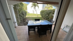 En patio med et glasbord og stole, omgivet af en hvid mur og udsigt til et grønt landskab.