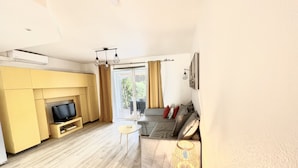 En moderne stue med et fladskærms-tv, en sofa, et lille bord og en lampe.