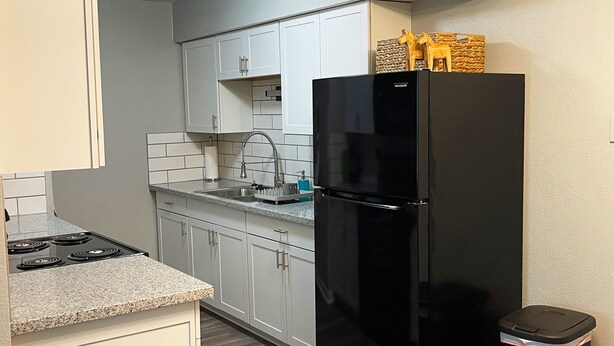 A kitchen with white cabinets, a black refrigerator, a gas stove, and a trash bin. - The Ingrid - Entire 2 Bedroom Apt in Quilt Town, USA (Hamilton)