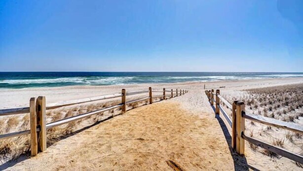 A sandy beach path leading to the ocean with wooden railings.