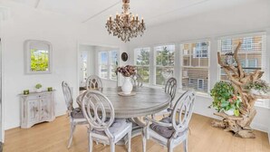 A dining area with a round table, white chairs, a chandelier, and a rustic plant stand.