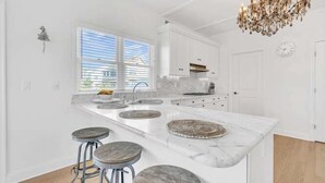 A modern kitchen with white cabinetry, a marble countertop, and a chandelier.