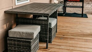 A wooden deck with a table and two wicker chairs with cushions.