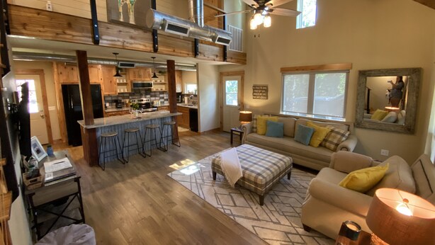A spacious living area with a high ceiling, a kitchen with modern appliances, and a cozy seating area with a sofa and ottoman.