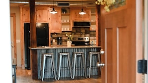 A modern kitchen with wooden cabinets, a central island with bar stools, and a hanging light fixture.