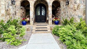A stone building with a central entrance, flanked by two large flower pots and a wooden chair. - Riverfront Mansion with Indoor Pool, Private Pond, and Hot Tub on 16 Acre Ranch (Hamilton)