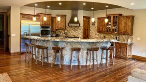 A kitchen with a curved island, wooden cabinets, and a stone backsplash. - Riverfront Mansion with Indoor Pool, Private Pond, and Hot Tub on 16 Acre Ranch (Hamilton)