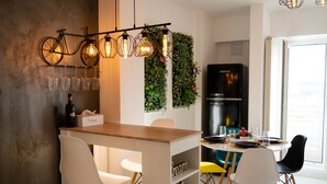 A modern kitchen with a wooden bar counter, white chairs, a black refrigerator, and a bicycle wall decoration.