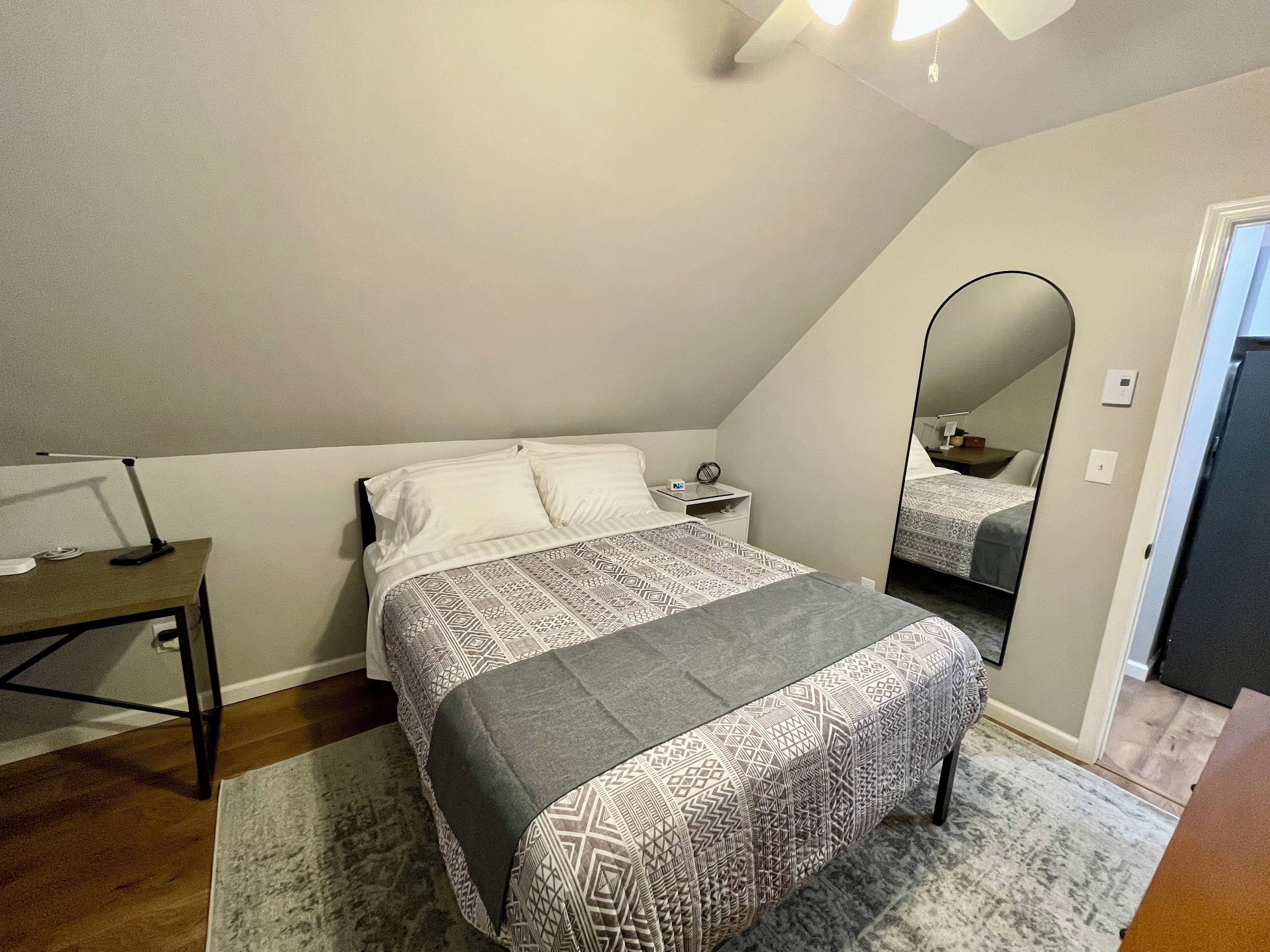 Un dormitorio con cama, mesita de noche, lámpara y espejo.