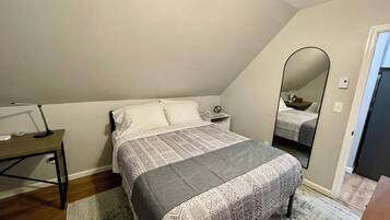 Un dormitorio con cama, mesita de noche, lámpara y espejo.