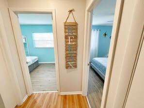 A hallway with a wooden wall decoration spelling "RELAX" and a blue room with a bed and a window.