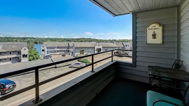 A balcony with a view of a parking lot and buildings, a framed sign on the wall, and a table with chairs. - Brown Family Condo - Top Floor Views - Boat Slip (Wisconsin Dells)