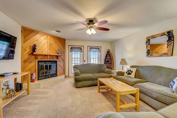 A cozy living room with a fireplace, a ceiling fan, and a television.