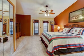 Ein Schlafzimmer mit einem großen Bett, einem Deckenventilator, einem Schminktisch, einem Spiegel und einer Tür zu einem weiteren Raum.
