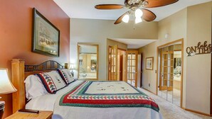 A bedroom with a bed, a desk, a lamp, a ceiling fan, and a door leading to another room. - Brown Family Condo - Top Floor Views - Boat Slip (Wisconsin Dells)