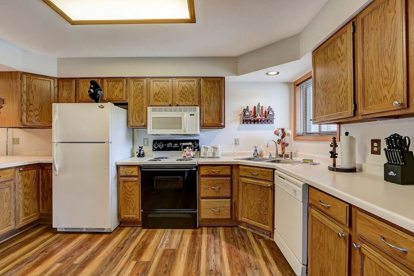 A kitchen with wooden cabinets, a white refrigerator, a microwave, an oven, and a sink.