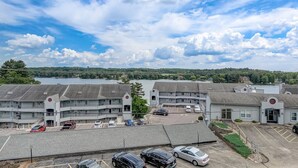 A multi-story motel with a parking lot, a small building with a sign, and a lake in the background. - Brown Family Condo - Top Floor Views - Boat Slip (Wisconsin Dells)