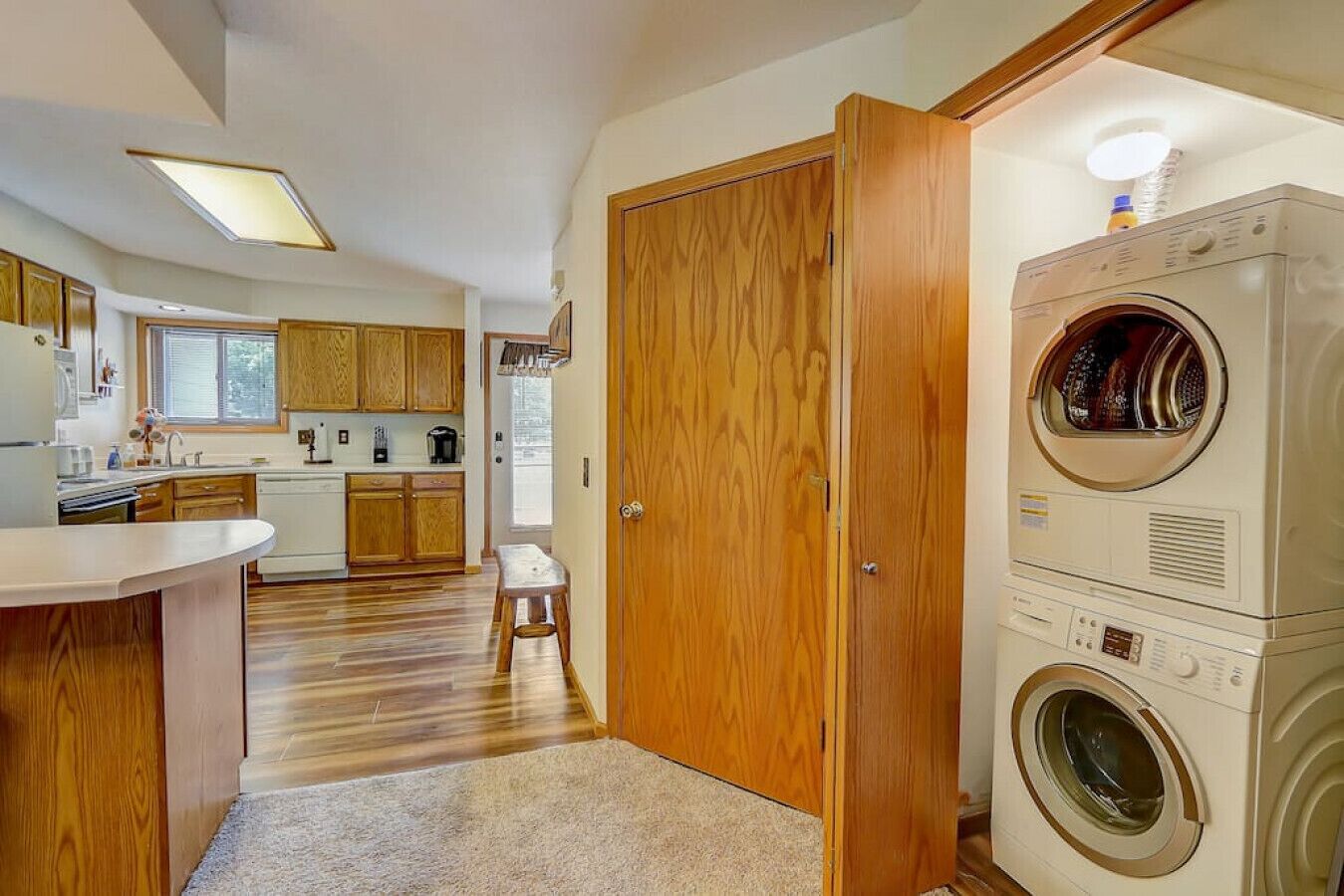 A compact kitchen with wooden cabinets, a built-in washing machine, and a small stool.