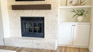 A living room with a stone fireplace, a flat-screen TV mounted above it, and a white cabinet with decorative items. - Newly Renovated from Top to Bottom! (Grand Lake)