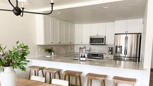 A modern kitchen with white cabinets, a stainless steel refrigerator, and a central island with stools. - Newly Renovated from Top to Bottom! (Grand Lake)