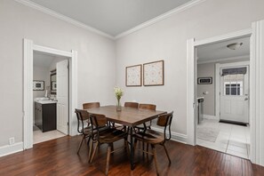A dining room with a wooden table and chairs, a vase with flowers, and framed artwork on the wall.